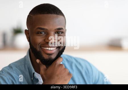 Gros plan d'un homme afro-américain souriant touchant la barbe Banque D'Images