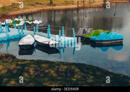 Bateaux et pédalos amarrés au quai sur le lac calme. Concept de service de location, d'affaires touristiques, d'activités de loisirs et de loisirs de plein air. Banque D'Images