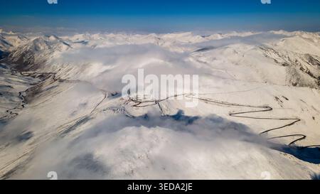 Vue aérienne de la route de montagne sinueuse au col de Babusar entourée de sommets enneigés et d'épais nuages blancs sous un ciel bleu clair Babusar, KPK, P. Banque D'Images