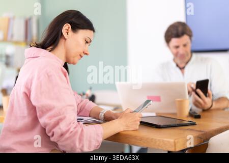 Femme adulte assise avec smartphone pendant la pause au bureau Banque D'Images