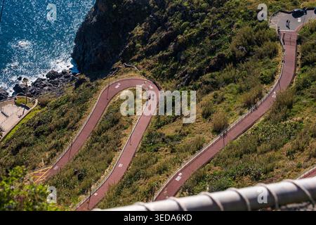 Vue aérienne des sentiers de randonnée pavés rouges sinueux creusés dans des falaises verdoyantes surplombant l'océan turquoise à Madère, au Portugal. Populaire Banque D'Images