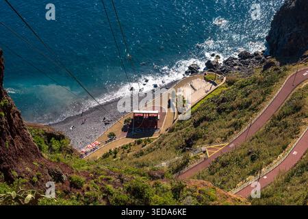 Plage côtière pittoresque nichée dans les falaises spectaculaires de Madère, Portugal. La perspective aérienne montre la station de téléphérique, le rivage sablonneux, turquoise Banque D'Images