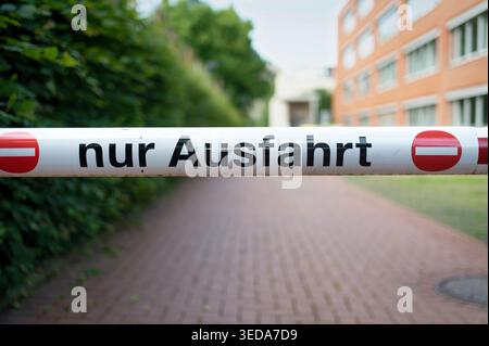 Une barrière blanche traversant une allée pavée avec texte allemand « nur Ausfahrt » et symboles « no entry ». Haie verte en arrière-plan Banque D'Images