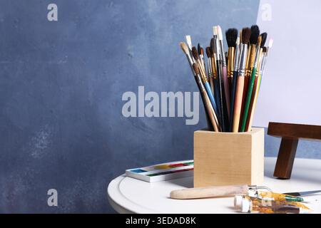 Pinceaux, couteau, peintures et chevalet avec toile sur table près du mur bleu. Espace pour le texte Banque D'Images