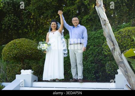 Homme asiatique senior, femme mature debout sur les marches, mariée dans la robe de mariée tenant le bouquet et le voile Banque D'Images