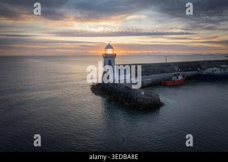 Vue aérienne du phare de Balbriggan au bout d'une jetée de pierre avec un bateau rouge amarré lors d'un lever de soleil vibrant Balbriggan, comté de Dublin, Irlande. Banque D'Images