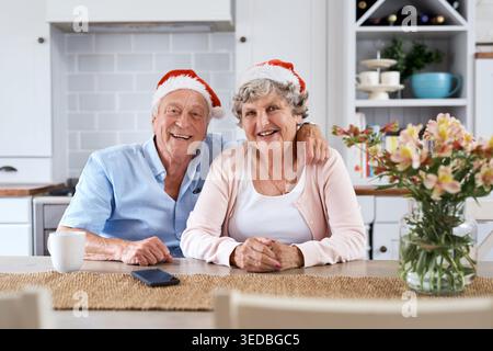 Noël, portrait et couple senior à la maison, sourire et se lier ensemble avec la saison des fêtes. Chapeaux de Noël, vieil homme et femme dans la cuisine, amour et Banque D'Images