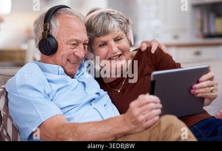 Casque, détente et vieux couple à la maison, tablette pour le divertissement en ligne et l'écoute de l'audio. Pensionné, homme senior et femme heureuse dans le salon Banque D'Images