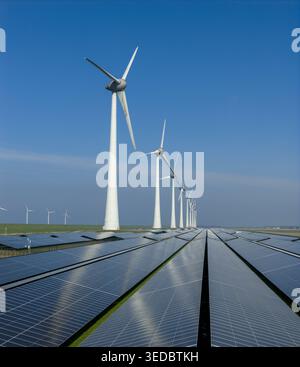 Vue aérienne d'une rangée d'éoliennes debout au-dessus d'un vaste champ de panneaux solaires sous un ciel bleu clair aux pays-Bas. Banque D'Images