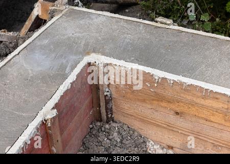 Coin d'une semelle en béton et d'un coffrage en bois sur un chantier de construction résidentielle montrant du ciment fraîchement coulé, de l'excavation du sol et de la base structurelle p Banque D'Images
