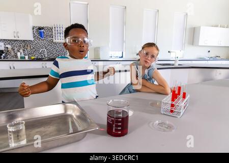 Des camarades de classe d'âge scolaire portant des lunettes faisant des expériences dans le laboratoire de l'école avec un bécher, des tubes à essai Banque D'Images