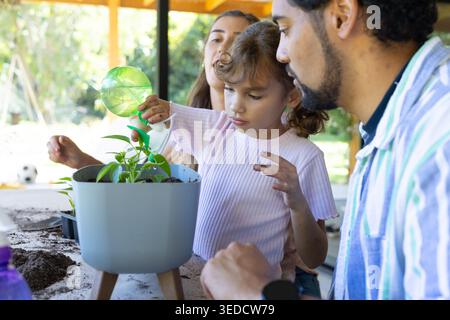 Famille afro-américaine guidant la fille de l'enfant versant de l'eau dans la jardinière sur le porche avec canette verte Banque D'Images