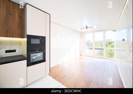 Appartement contemporain avec tour de four intégrée, grande fenêtre ensoleillée et espace de vie vide. Intérieur élégant avec lignes épurées, parquet et concept immobilier haut de gamme Banque D'Images