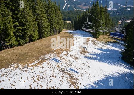 Télésiège vide sur la piste de ski avec la fonte de la neige, paysage de forêt de montagne au printemps, perspective aérienne du terrain de la station avec des taches d'herbe et le ciel clair Banque D'Images