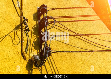 Une vue artistique des fils électriques contre un mur jaune éclatant. L'image capture les détails complexes de l'infrastructure urbaine, mettant en valeur Connect Banque D'Images