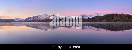 Vue panoramique d'un lever de soleil d'hiver avec des montagnes enneigées reflétant Derwentwater dans le Lake District, Royaume-Uni. Banque D'Images