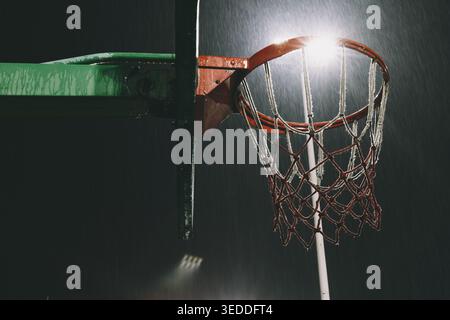 Panier de basket-ball imbibé de pluie sous les lumières du stade la nuit, gros plan avec des gouttelettes d'eau et givré Banque D'Images