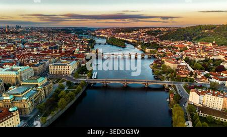 Vue aérienne de la rivière Vltava qui traverse la vieille ville historique avec ses ponts emblématiques et son architecture aux toits rouges pendant l'heure dorée à Prague Banque D'Images
