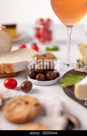Une table est mise en place avec divers aliments et boissons. Il y a des olives dans un petit bol, du pain tranché, différents types de fromage et des biscuits. Un verre o Banque D'Images