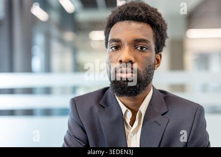 Jeune homme d'affaires avec origine ethnique et barbe debout directement à la caméra, montrant la confiance et le professionnalisme dans un environnement d'entreprise contemporain Banque D'Images