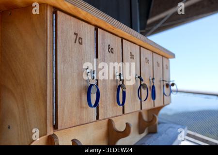 Une rangée de casiers en contreplaqué numérotés dans une installation moderne. Chaque casier a une clé insérée avec un porte-clés bracelet en caoutchouc bleu. Concept de stockage sécurisé Banque D'Images