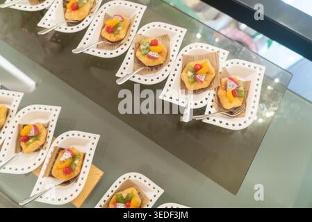 Un superbe affichage de desserts colorés magnifiquement disposés sur d'élégants plateaux blancs. Chaque friandise est composée d'un délicieux mélange de fruits frais Banque D'Images