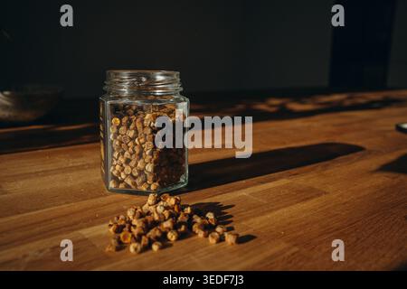 Pot en verre de pain d'abeille avec des granulés renversés sur une table. Produit apicole naturel, riche en vitamines, superaliment biologique et concept de nutrition saine Banque D'Images