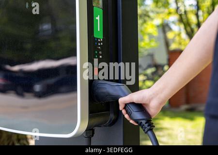 Branchement manuel du câble dans le chargeur EV. Gros plan d'une main connectant un câble de recharge de véhicule électrique à une station de recharge extérieure publique. Banque D'Images