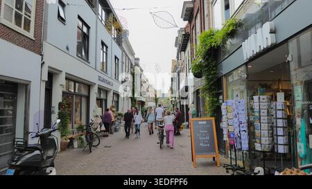 Les gens se promènent dans une rue commerçante étroite bordée de petites boutiques et de devantures de magasins dans un cadre urbain animé. Banque D'Images