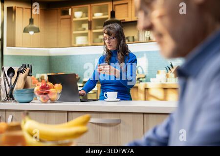 Femme mature complète la commande en ligne avec une carte de débit, en sélectionnant les essentiels quotidiens et les ustensiles de cuisine sur le site e-commerce. L'acheteur féminin apprécie la livraison à domicile et les décisions d'épicerie. Banque D'Images
