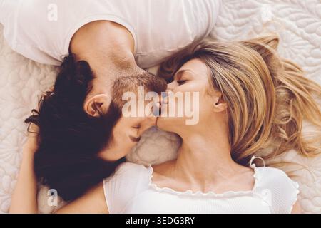 Couple partageant un baiser tout en étant allongé sur un lit dans une salle lumineuse pendant l'après-midi Banque D'Images