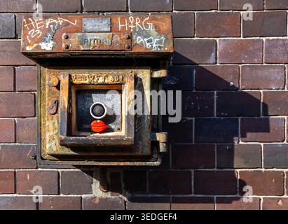 Gros plan d'un boîtier de bouton d'urgence industriel endommagé monté sur un mur de briques carrelées. VEB, DDR, GDR, usage éditorial uniquement. Banque D'Images