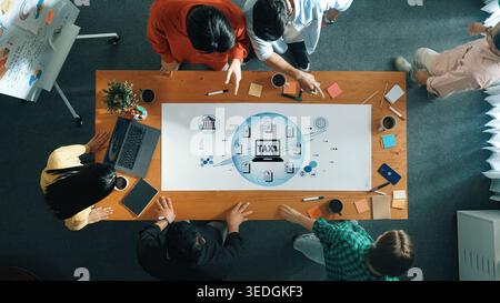Collaboration dans un cadre de bureau avec une équipe diversifiée discutant des concepts fiscaux avec des graphiques et des notes sur table Fluxor. Banque D'Images