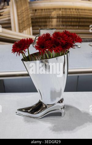 Fleurs rouges dans un vase métallique moderne en forme de chaussure à talons hauts. Arrangement floral élégant et concept de décoration contemporaine. Banque D'Images