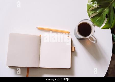 Ouvrez le cahier avec le café et la feuille de monstera sur la table Banque D'Images