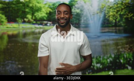 Jeune homme afro-américain pointe le doigt et tient le ventre dans un ensemble de forêt tout en souriant à la caméra ; joie. Banque D'Images
