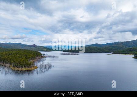 Vue aérienne d'un lac tranquille avec des arbres morts exposés s'élevant de l'eau près d'une forêt luxuriante avec des collines ondulantes. Banque D'Images