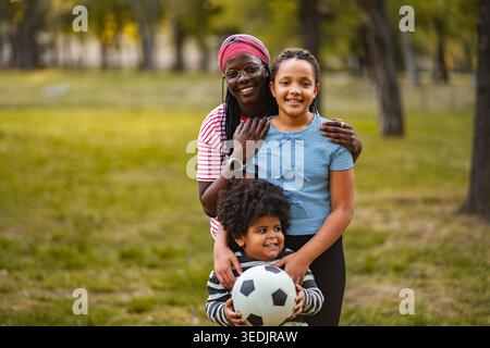 Mère afro-américaine et enfants heureux jouant au football en plein air Banque D'Images