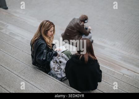 Élèves du secondaire assis sur des marches extérieures étudiant avec des sacs à dos dans un cadre urbain Banque D'Images