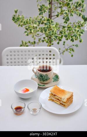 un petit-déjeuner typique de style kopitiam se compose de kopi susu ou café au lait sucré, de toasts kaya et d'œufs durs, servis dans une table blanche Banque D'Images
