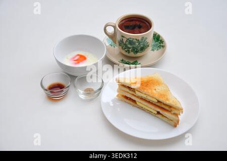 un petit-déjeuner typique de style kopitiam se compose de kopi susu ou café au lait sucré, de toasts kaya et d'œufs durs, servis dans une table blanche Banque D'Images