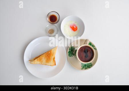 un petit-déjeuner typique de style kopitiam se compose de kopi susu ou café au lait sucré, de toasts kaya et d'œufs durs, servis dans une table blanche Banque D'Images