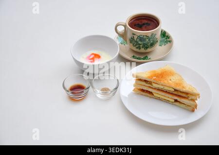 un petit-déjeuner typique de style kopitiam se compose de kopi susu ou café au lait sucré, de toasts kaya et d'œufs durs, servis dans une table blanche Banque D'Images