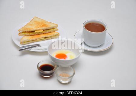 un petit-déjeuner typique de style kopitiam se compose de kopi susu ou café au lait sucré, de toasts kaya et d'œufs durs, servis dans une table blanche Banque D'Images