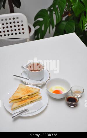 un petit-déjeuner typique de style kopitiam se compose de kopi susu ou café au lait sucré, de toasts kaya et d'œufs durs, servis dans une table blanche Banque D'Images