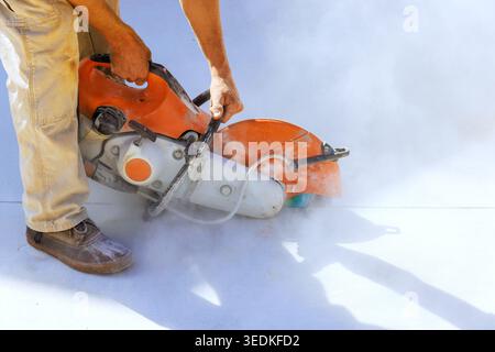 Le travailleur a utilisé une scie à béton pour couper la surface sur le site tandis que des nuages de poussière se forment autour de la zone à partir de l'action. Banque D'Images
