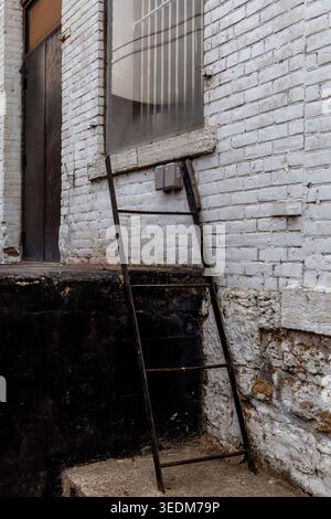 Dubuque, Iowa, États-Unis - 25 avril 2026 : échelle en métal rouillé appuyée contre un bâtiment industriel en briques blanches altérées dans le centre-ville de Dubuque, Iowa Banque D'Images