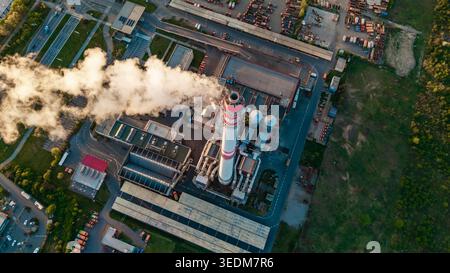 Vue aérienne des objets d'infrastructure Malesice avec une grande cheminée émettant de la fumée blanche, des bâtiments industriels et des parkings au coucher du soleil à Hlavni me Banque D'Images