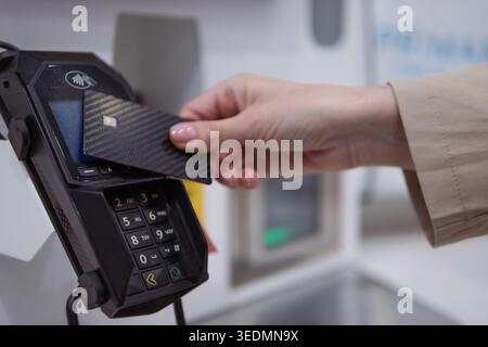 Main tenant une carte de crédit élégante en fibre de carbone tapotée contre un terminal POS pour un paiement sans contact sécurisé, illustrant le commerce de détail sans espèces moderne Banque D'Images