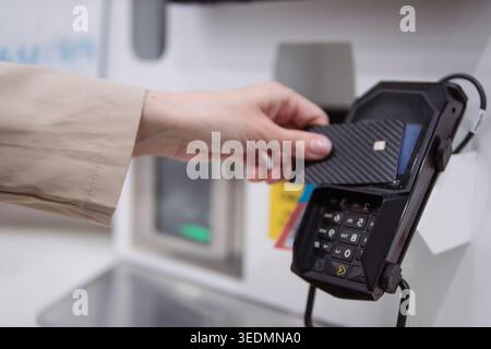 Personne complétant de manière transparente une transaction sans contact en tapant commodément une carte de crédit en fibre de carbone élégante sur un terminal, mettant en valeur la facilité et Banque D'Images